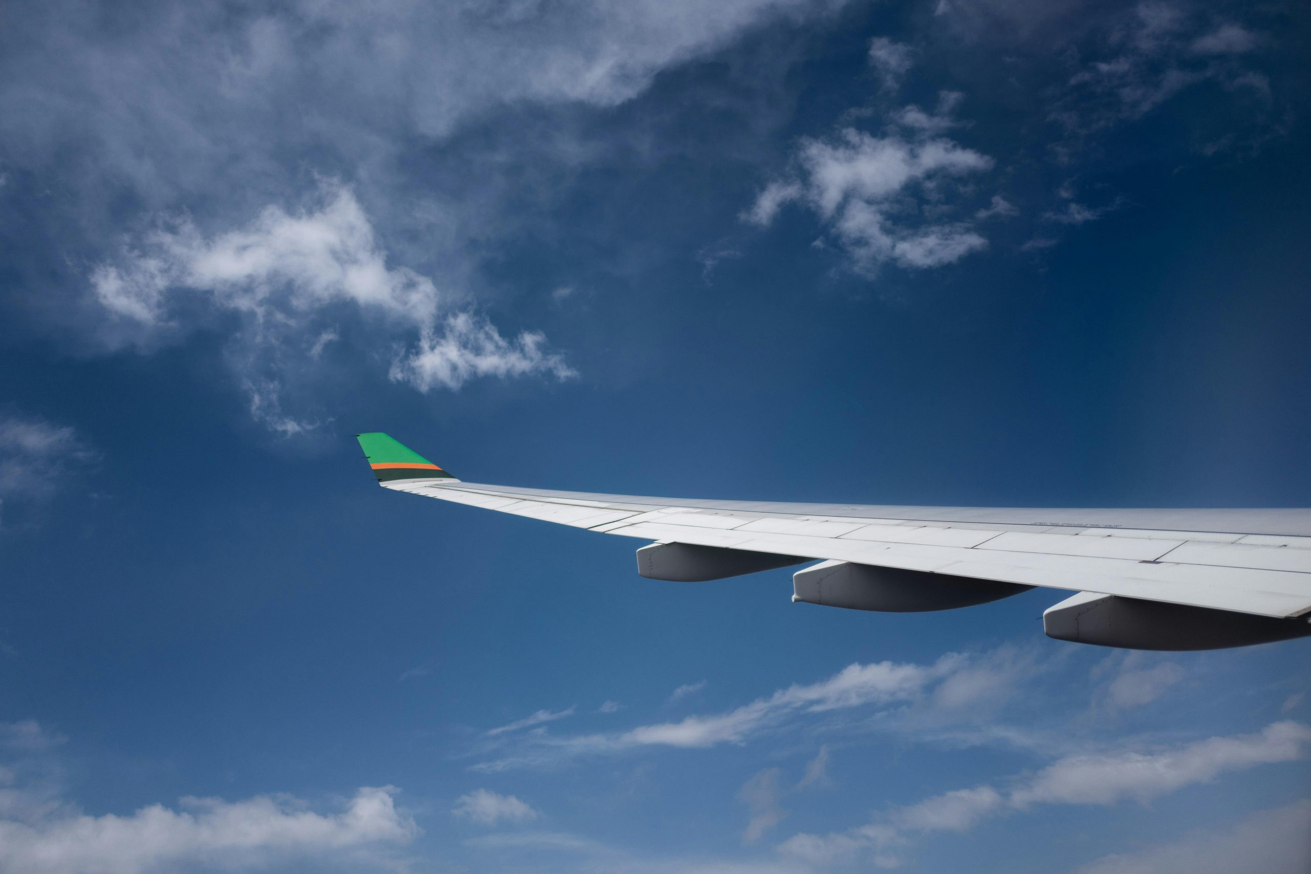 View of an airplane wing soaring through a clear blue sky with white clouds.