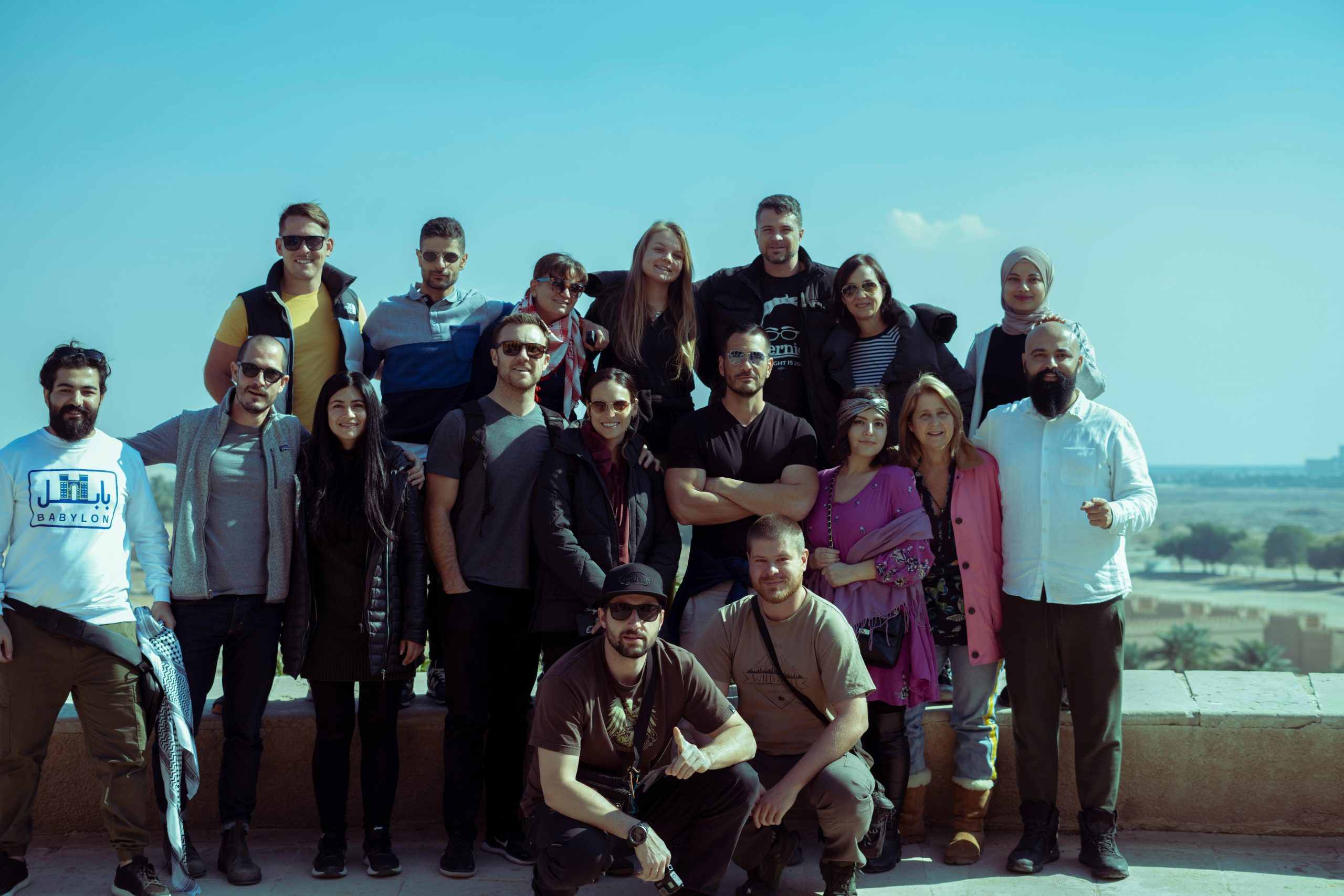 A diverse group of adults smiling and posing outdoors in Baghdad, Iraq.